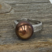 Load image into Gallery viewer, There is only one of these and the size is adjustable.
This exquisite ring features a superb Round 12mm Freshwater pearl that is a natural Chocolate color with Gold hues.
It is just divine with baget cut white cubic zirconia set along both shoulders of this 925 Sterling Silver, non tarnish finish ring
Size is adjustable