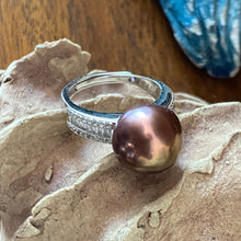Load image into Gallery viewer, There is only one of these and the size is adjustable.
This exquisite ring features a superb Round 12mm Freshwater pearl that is a natural Chocolate color with Gold hues.
It is just divine with baget cut white cubic zirconia set along both shoulders of this 925 Sterling Silver, non tarnish finish ring
Size is adjustable