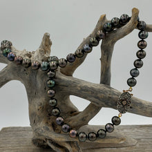Load image into Gallery viewer, This glamourous Black Freshwater pearl strand features dark round pearls with Green and Purple hues, 8-8.5mm in size.
The highlight is the intricate goddess like Rose Gold and Sterling silver clasp that is a feature of this strand and designed to be worn to see.
Total length including clasp is 48cm