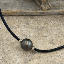 Load image into Gallery viewer, Very large stunning Tahitian South Sea pearl featured on black leather with a stainless steel magnetic clasp and rondels either side of the pearl.
This pearl is Round, 15.5mm in size and dark green with a chocolate color hue to it.
It has light natural birthmarks which add to its character.
The necklet is 52cm in length so perfect as a unisex necklet.
J3571