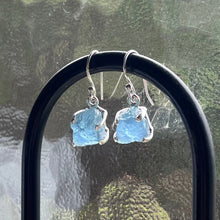 Load image into Gallery viewer, <p>Sterling silver claw set shepherds hook style earrings featuring stunning Rough cut Aquamarine gemstones</p> <p>The stones vary in shape but are roughly rectangle and 11 x 12mm in size</p> <p>Team your aquamarine earrings with an aquamarine necklace for a WOW effect</p>