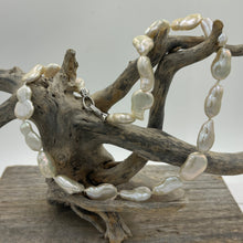 Load image into Gallery viewer, This gorgeous seedless pearl strand looks a little like pear shapes. It features white with high lustre, 12 x 20mm pearls that have no nuclei so are quite flat in shape. They sit perfectly on any neck. This strand is fully knotted and features a rhodium coated non tarnish Sterling silver clasp. The length including clasp is 44cm.