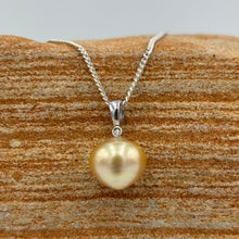 Load image into Gallery viewer, This Golden South Sea pearl pendant is set on 925 Sterling silver with a single bezel set cubic zirconia for subtle bling. The setting has a non tarnish finish.
The pearl is Button in shape, 11mm in size and a warm deep gold colour.
The lustre is Good with some light 'birthmarks'
Chain included is Base metal only
J3231