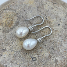 Load image into Gallery viewer, These elegant and classic Hook earrings are Sterling Silver and rhodium coated for a non tarnish finish and they feature a single claw set cubic zirconia above each pearl.
The pearls are tear drop shape, 9 x 12mm in size and white with pink hues in colour.
Also available with Black or Pink pearls to order