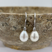 Load image into Gallery viewer, These elegant and classic Hook earrings are Sterling Silver and rhodium coated for a non tarnish finish and they feature a single claw set cubic zirconia above each pearl.
The pearls are tear drop shape, 9 x 12mm in size and white with pink hues in colour.
Also available with Black or Pink pearls to order
