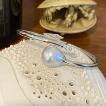 Load image into Gallery viewer, Sterling Silver solid bangle featuring an Australian South Sea Pearl and a bezel set cubic zirconia at either end
This stunning pearl is an Australian South Sea pearl, Circle Drop in shape and 13.8 x 15mm in size. It has high lustre and light natural birthmarks
It is White with Silver Pink hues and is featured on this non tarnish wrap bangle
J3508