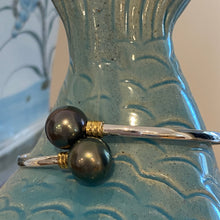Load image into Gallery viewer, This double pearl bangle is unique with its Sterling Silver bangle featuring a gold plated rib at each pearl. The pearls are Round in shape, 11mm in size and are a natural unique Aubergine in color. They both have Good lustre.
It is featured on this non tarnish wrap bangle
J3515