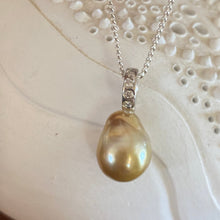 Load image into Gallery viewer, This Fijian South Sea pearl pendant enhancer is set on 925 Sterling silver with four channel set cubic zirconia for added bling. The setting has a non tarnish finish.
It is quite rare for a Blacklip pearl oyster to produce a gold pearl but in the waters of Fiji anything is possible due to the mix of coral and estuaries. This pearl is deep Gold with a green hue in colour, and is Semi Baroque in shape. The size of this unique pearl is 10.5 x 14mm.
The lustre is Excellent and the birthmarks
