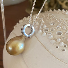 Load image into Gallery viewer, This Fijian South Sea pearl pendant enhancer is set on 925 Sterling silver with four channel set cubic zirconia for added bling. The setting has a non tarnish finish.
It is quite rare for a Blacklip pearl oyster to produce a gold pearl but in the waters of Fiji anything is possible due to the mix of coral and estuaries. This pearl is deep Gold with a green hue in colour, and is Semi Baroque in shape. The size of this unique pearl is 10.5 x 14mm.
The lustre is Excellent and the birthmarks