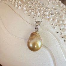 Load image into Gallery viewer, This Fijian South Sea pearl pendant enhancer is set on 925 Sterling silver with four channel set cubic zirconia for added bling. The setting has a non tarnish finish.
It is quite rare for a Blacklip pearl oyster to produce a gold pearl but in the waters of Fiji anything is possible due to the mix of coral and estuaries. This pearl is deep Gold with a green hue in colour, and is Semi Baroque in shape. The size of this unique pearl is 10.5 x 14mm.
The lustre is Excellent and the birthmarks