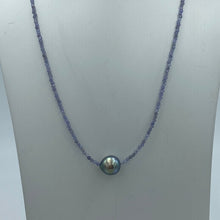 Load image into Gallery viewer, Tahitian pearl necklace with faceted Tanzanite gemstones and a sterling silver peanut clasp. This necklace features a peacock coloured Tahitian pearl, drop shape, and 9.5mm x 10.5mm in size. It is white with silver hues in colour. Good lustre and light natural 'birthmarks'. Beautiful 2mm Tanzanite and the overall length, including clasp, is 45cm. J3373