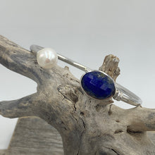 Load image into Gallery viewer, This bangle is a colorful addition to any collection featuring a facetted blue Lapis gemstone and a white Freshwater pearl, Button in shape and 10mm in size

It is made from 925 sterling silver and has a non tarnish finish and is an adjustable size
