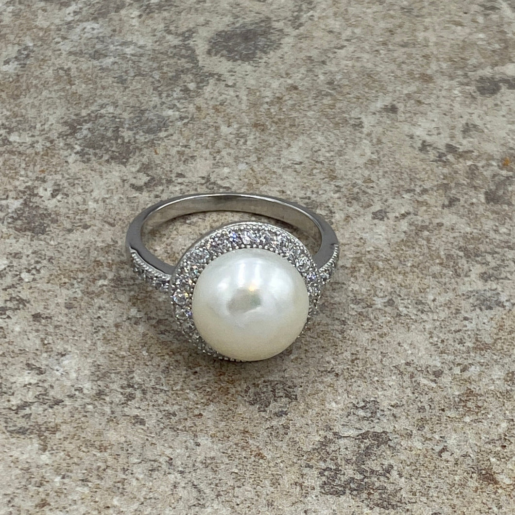 Stunning Sterling silver ring featuring an 11mm White freshwater  Button shape pearl cradled in a Halo of  Cubic Zirconia which also extend down the shank of the ring.

This ring has a non tarnish finish and comes in various sizes